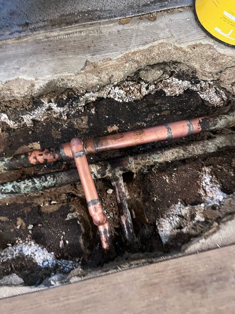 Copper heating pipes and fittings exposed in a trench cut through a concrete floor