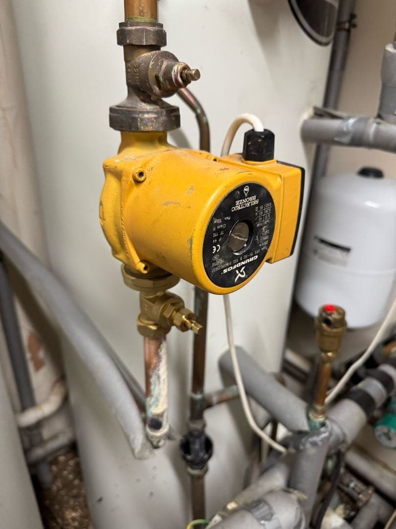 A yellow hot-water circulating pump with brass unions and valves above and below it