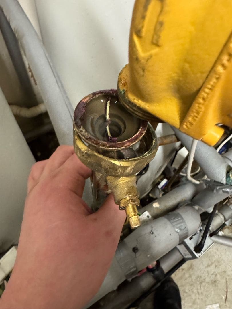 A hand holding an opened brass pump union below a yellow circulating pump
